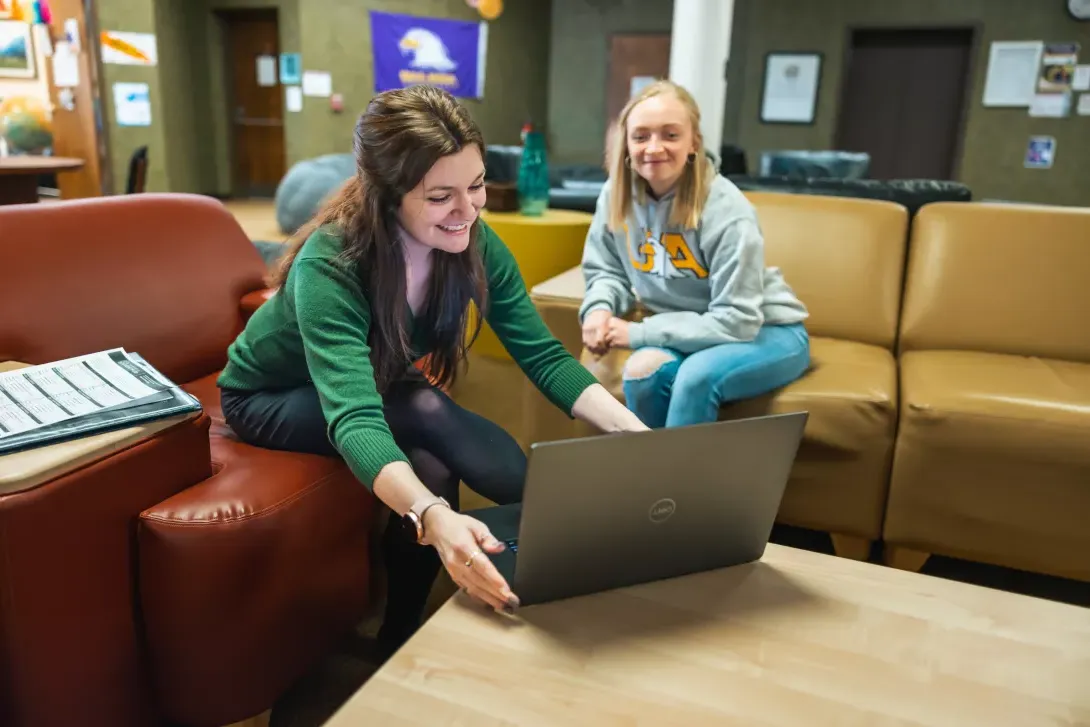 Students sitting on bench in dorm lobby working on a laptop computer